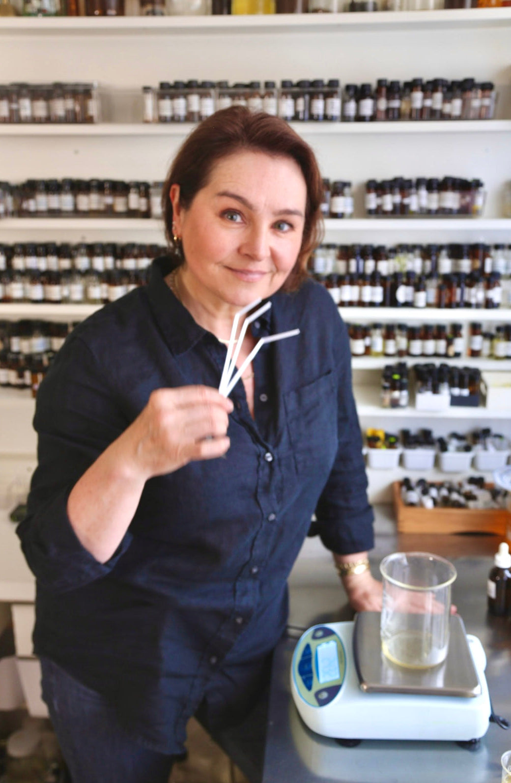 Wedding perfumer holding a blotter in a Scent laboratory setting with shelves of bottles in the background.